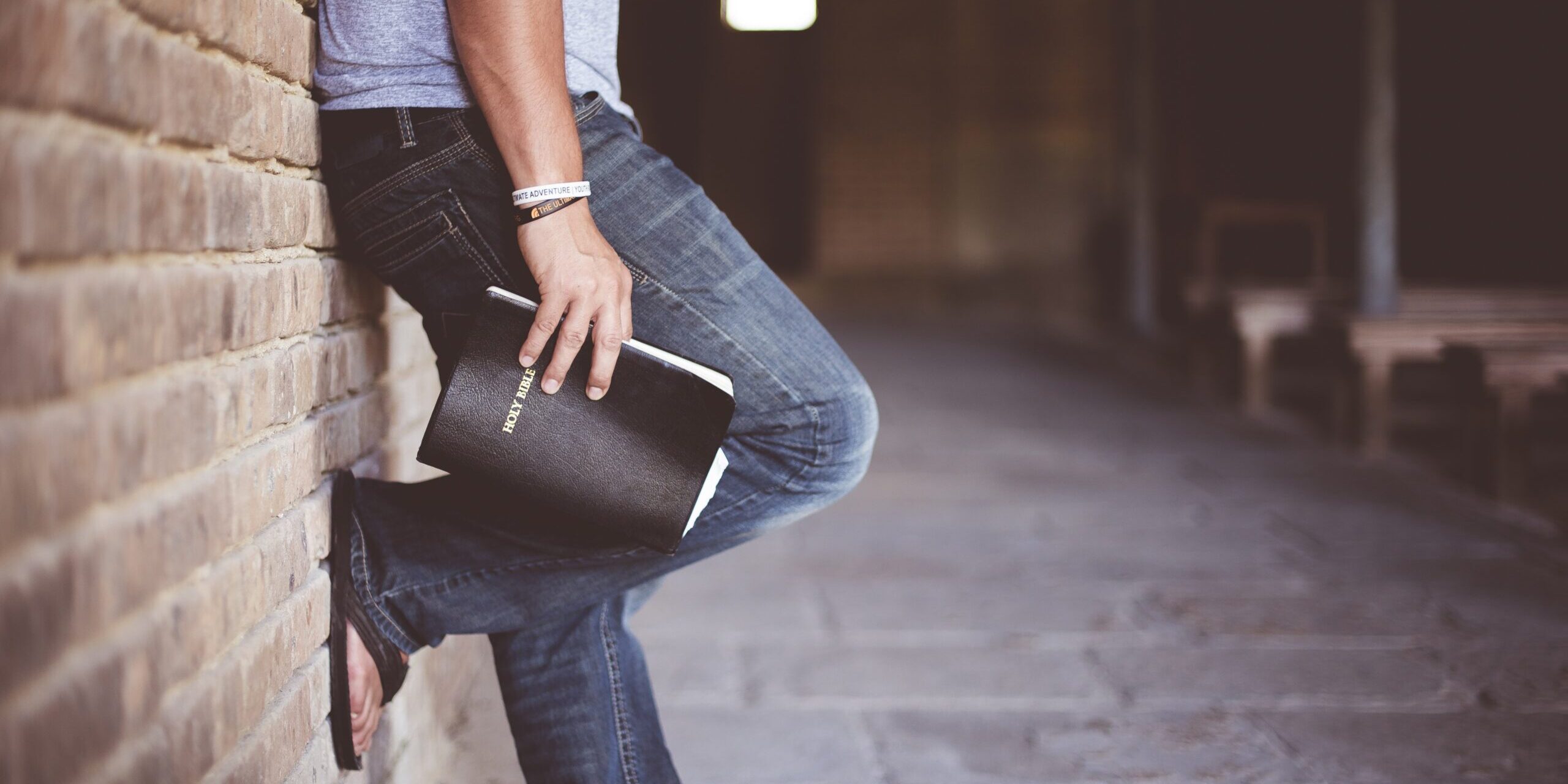 Bibel Billede af en person, lænet op af væggen i en kirkelignende bygning med en bibel i hånden